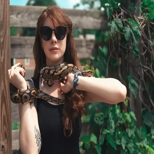 A woman safely holding a calm pet snake outdoors, illustrating the docile temperament detailed in our complete Ball Python Care Guide.